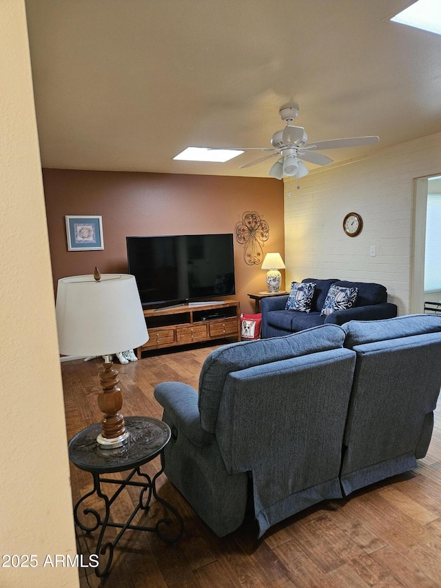 living room featuring wood finished floors, a ceiling fan, and a skylight