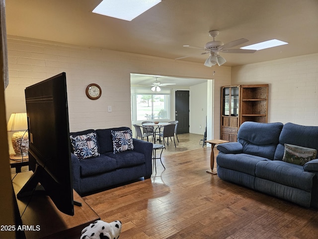 living area with wood finished floors, ceiling fan, and a skylight