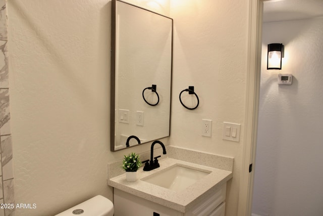 half bathroom featuring a textured wall, vanity, and toilet