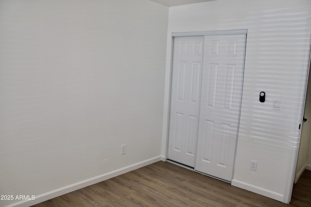 unfurnished bedroom featuring dark wood-style floors, a closet, and baseboards