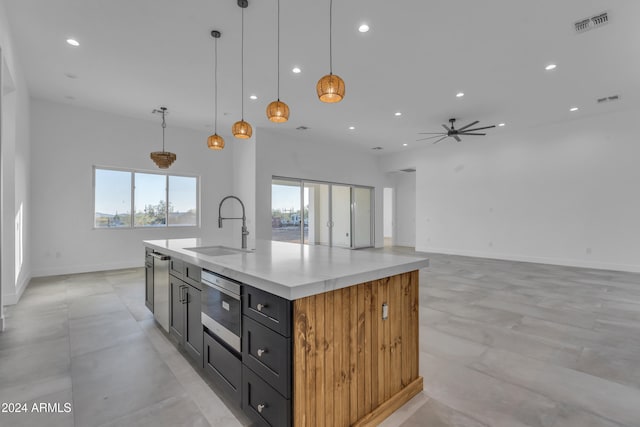 kitchen with ceiling fan, sink, hanging light fixtures, and a kitchen island with sink