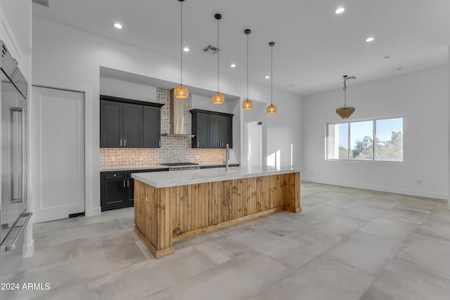 kitchen with a center island with sink, wall chimney range hood, hanging light fixtures, and tasteful backsplash