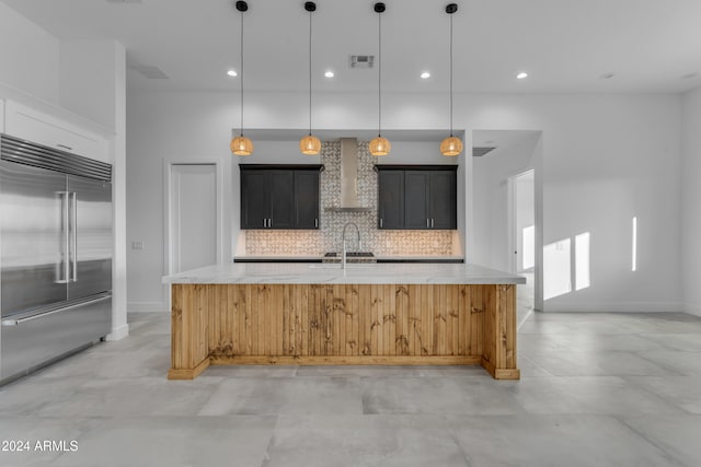 kitchen featuring backsplash, built in fridge, an island with sink, and hanging light fixtures