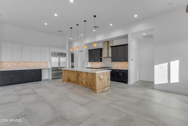 kitchen featuring a large island, wall chimney range hood, decorative light fixtures, decorative backsplash, and appliances with stainless steel finishes