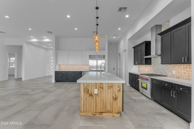 kitchen with wall chimney exhaust hood, premium appliances, a kitchen island with sink, sink, and hanging light fixtures