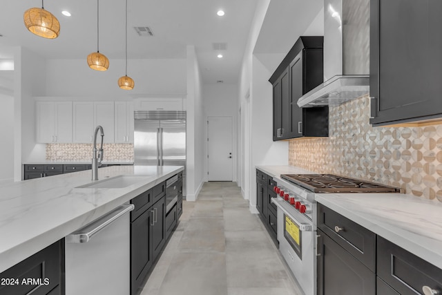 kitchen featuring high end appliances, wall chimney range hood, sink, tasteful backsplash, and decorative light fixtures