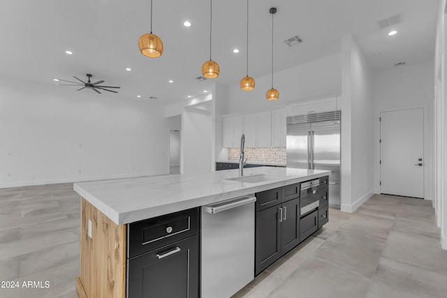 kitchen featuring backsplash, sink, hanging light fixtures, ceiling fan, and an island with sink