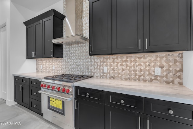 kitchen with light stone countertops, backsplash, designer stove, and wall chimney exhaust hood