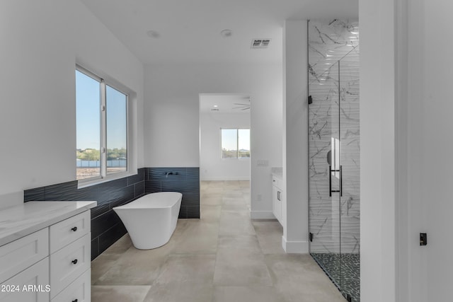 bathroom with vanity, separate shower and tub, tile walls, and a wealth of natural light