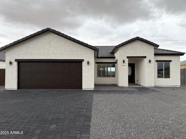 view of front of property with a garage, fence, a tiled roof, decorative driveway, and stucco siding