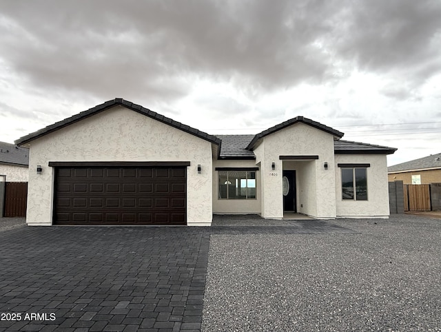 view of front facade featuring decorative driveway, a tile roof, stucco siding, fence, and a garage