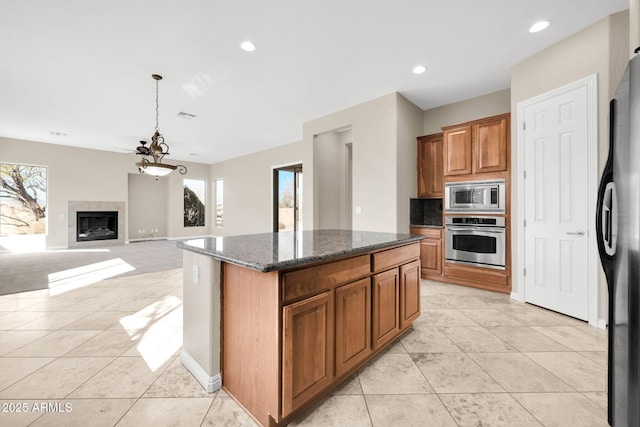 kitchen featuring dark stone countertops, stainless steel appliances, a center island, light tile patterned flooring, and decorative light fixtures