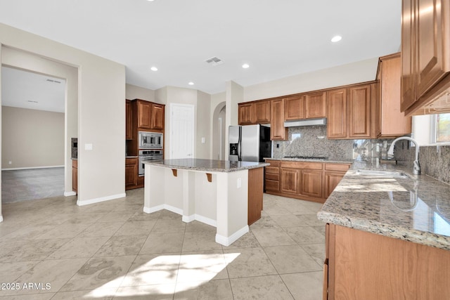 kitchen featuring sink, tasteful backsplash, appliances with stainless steel finishes, a kitchen island, and light stone countertops