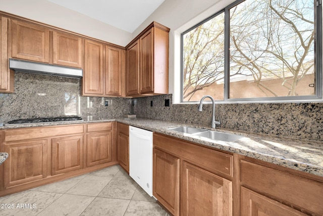 kitchen with stainless steel gas stovetop, sink, backsplash, light stone counters, and white dishwasher