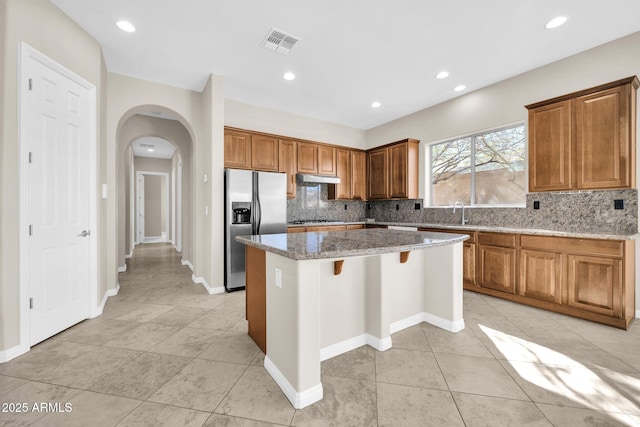 kitchen featuring a kitchen island, appliances with stainless steel finishes, a breakfast bar area, backsplash, and light stone countertops