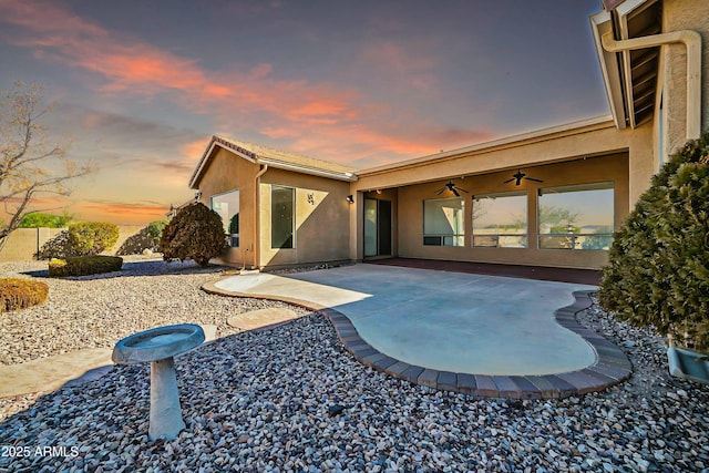 back house at dusk featuring ceiling fan and a patio area