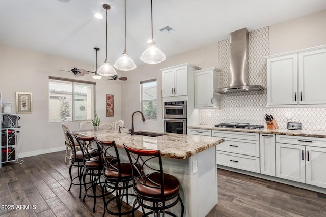 kitchen featuring sink, white cabinets, a kitchen island with sink, stainless steel appliances, and wall chimney exhaust hood