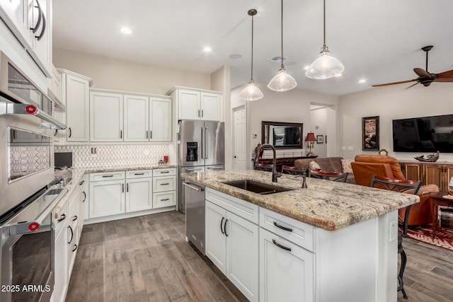 kitchen with decorative light fixtures, sink, white cabinets, light stone counters, and a center island with sink