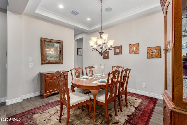 dining area featuring hardwood / wood-style flooring, ornamental molding, a raised ceiling, and a notable chandelier