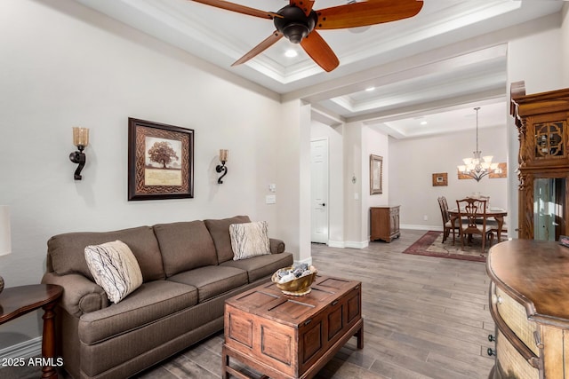 living room with a tray ceiling, wood-type flooring, ornamental molding, and ceiling fan with notable chandelier