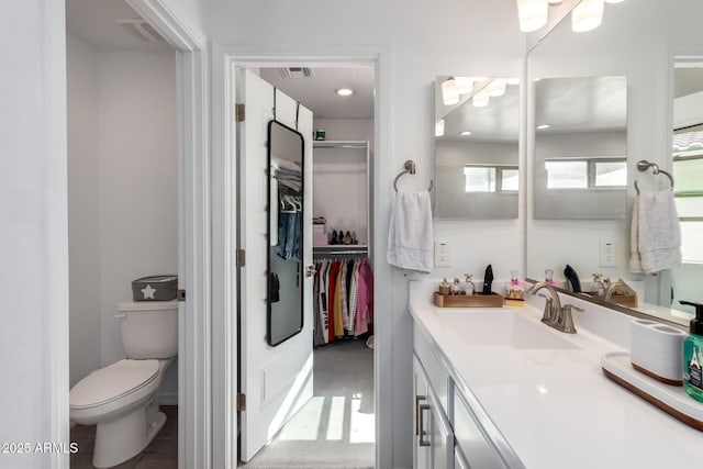 full bath with a walk in closet, toilet, visible vents, and vanity