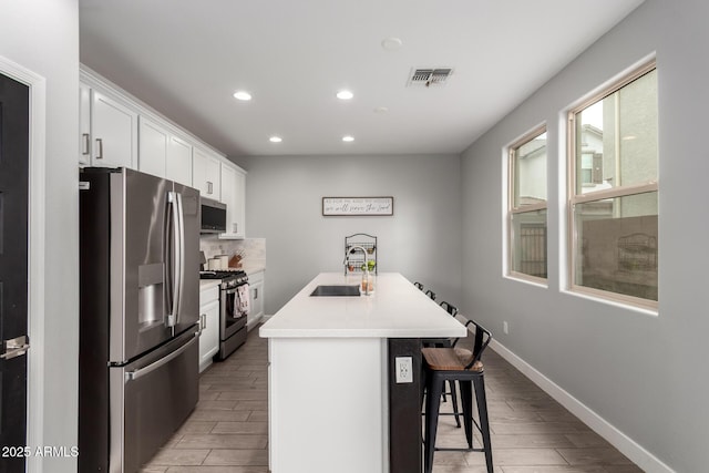 kitchen with an island with sink, light countertops, appliances with stainless steel finishes, white cabinetry, and a sink