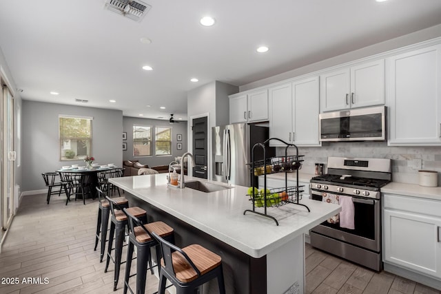 kitchen with visible vents, a sink, backsplash, stainless steel appliances, and light wood finished floors