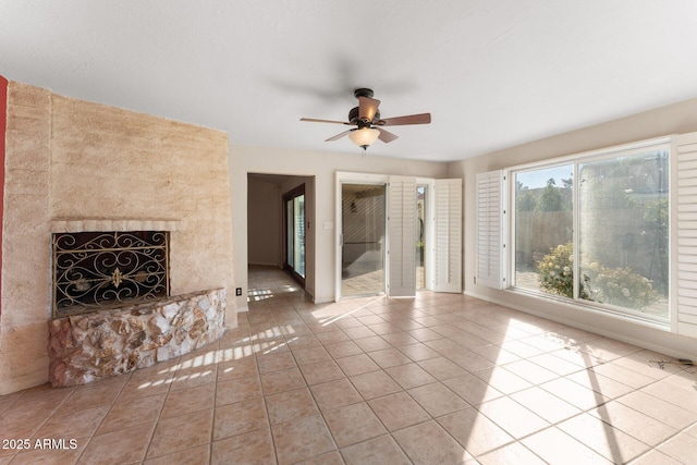 unfurnished living room with tile patterned flooring, a stone fireplace, and ceiling fan