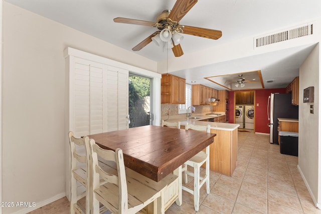 tiled dining space featuring sink, a tray ceiling, washer and dryer, and ceiling fan