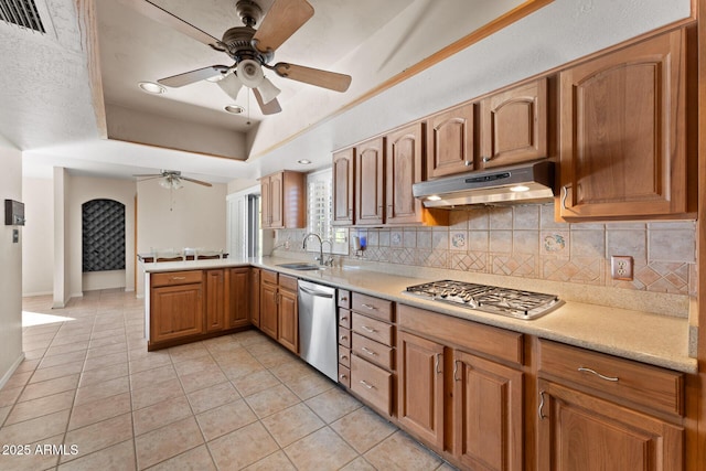 kitchen with sink, stainless steel appliances, a tray ceiling, light tile patterned flooring, and kitchen peninsula