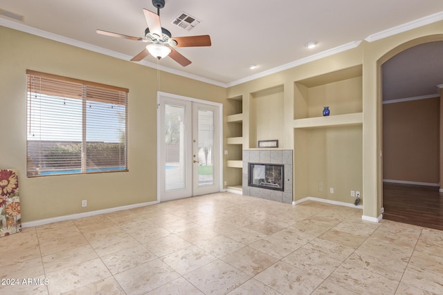 unfurnished living room featuring built in features, a tiled fireplace, ceiling fan, crown molding, and french doors