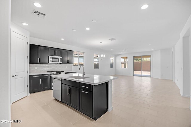 kitchen with sink, tasteful backsplash, a center island with sink, appliances with stainless steel finishes, and pendant lighting