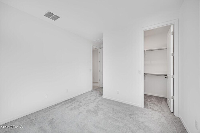 unfurnished bedroom with a walk in closet, light colored carpet, and a closet