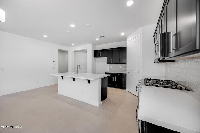 kitchen featuring a kitchen island with sink, backsplash, and range with gas cooktop