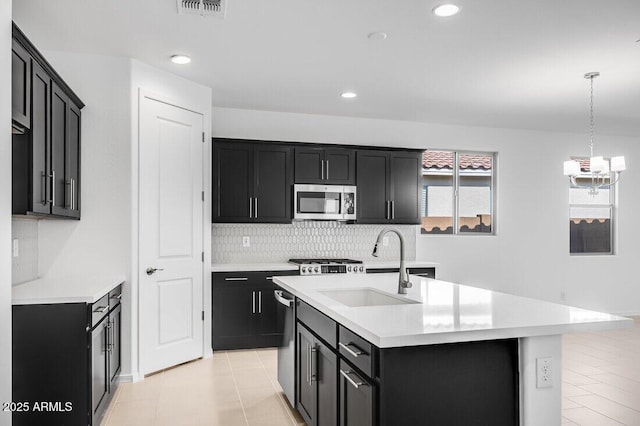 kitchen with sink, a kitchen island with sink, stainless steel appliances, tasteful backsplash, and decorative light fixtures