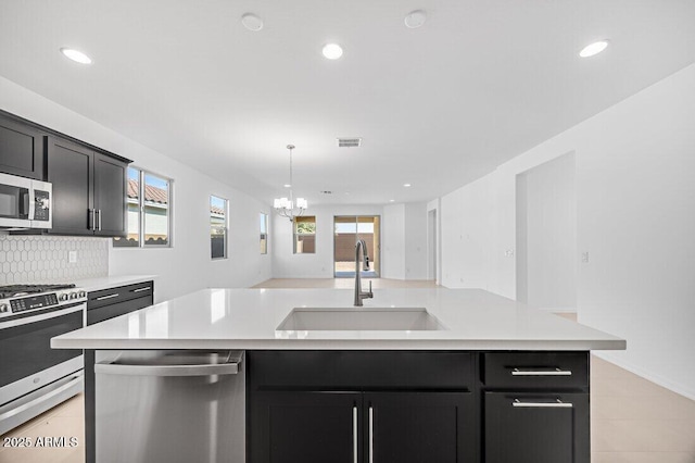 kitchen with light tile patterned flooring, sink, tasteful backsplash, a center island with sink, and appliances with stainless steel finishes