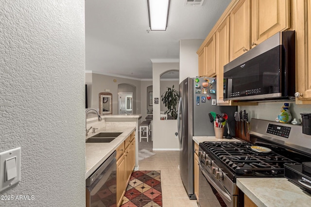 kitchen featuring light tile patterned floors, a sink, light countertops, appliances with stainless steel finishes, and light brown cabinetry