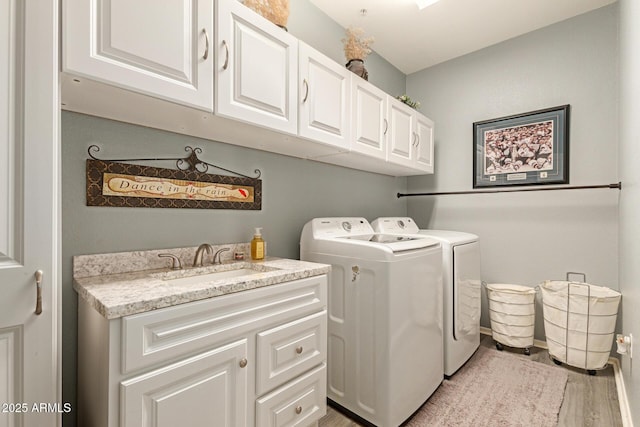 clothes washing area featuring light wood finished floors, washing machine and dryer, a sink, and cabinet space