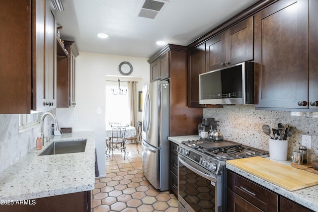 kitchen featuring light stone countertops, dark brown cabinetry, stainless steel appliances, decorative backsplash, and sink