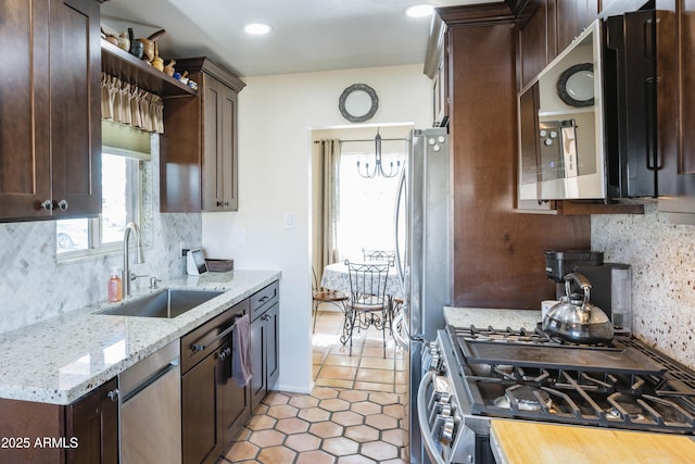 kitchen featuring appliances with stainless steel finishes, tasteful backsplash, sink, light stone counters, and dark brown cabinets