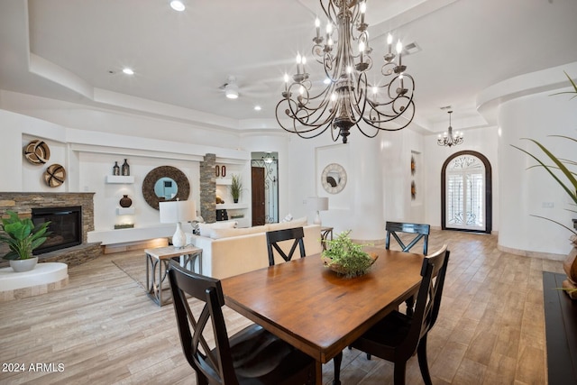 dining room featuring a raised ceiling, a stone fireplace, and light hardwood / wood-style floors