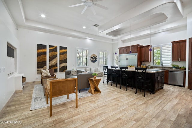 living room with a towering ceiling, a tray ceiling, ceiling fan, and light hardwood / wood-style floors