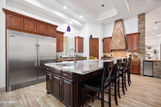 kitchen with a center island, sink, hanging light fixtures, built in refrigerator, and a breakfast bar area