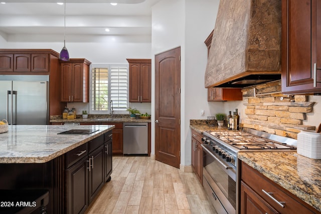 kitchen with sink, light stone counters, light hardwood / wood-style flooring, high quality appliances, and custom range hood