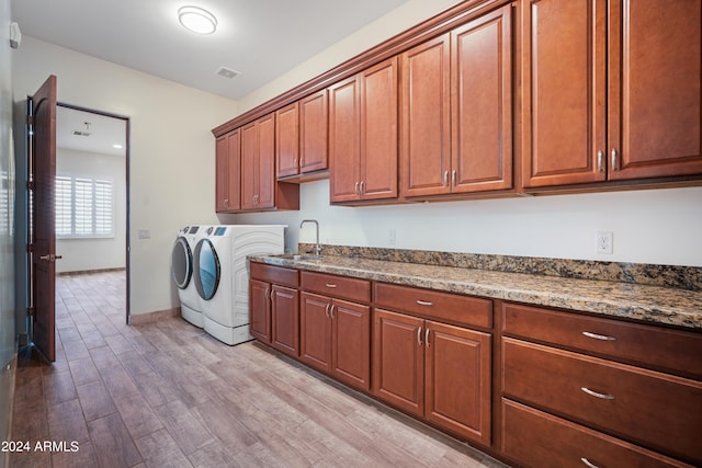 washroom featuring cabinets, sink, light hardwood / wood-style floors, and washing machine and clothes dryer