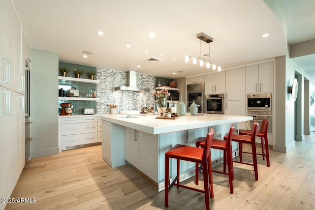 kitchen featuring decorative light fixtures, backsplash, a kitchen bar, a large island with sink, and wall chimney range hood