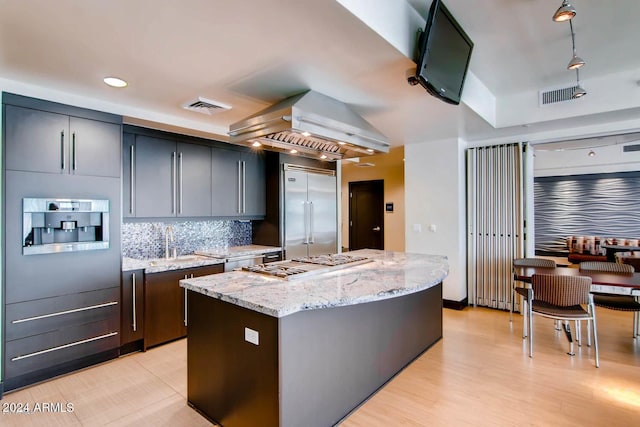 kitchen featuring range hood, stainless steel appliances, light stone countertops, a kitchen island, and decorative backsplash