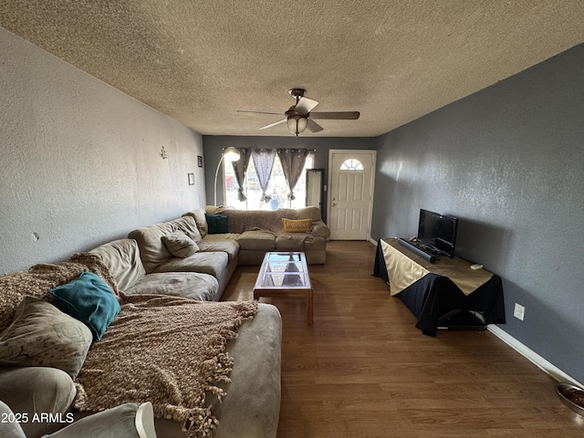 living room featuring a textured wall, wood finished floors, a ceiling fan, a textured ceiling, and baseboards