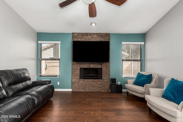 living area with plenty of natural light, baseboards, dark wood-type flooring, and a stone fireplace