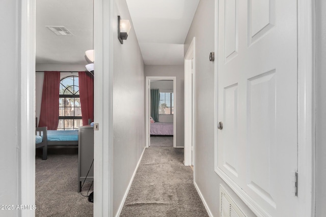 corridor featuring light carpet, baseboards, visible vents, and a wealth of natural light